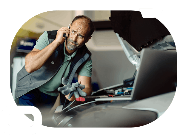 Mechanic with screwdriver in one hand and another hand raised to his ear, talking on the phone while looking at a car engine with the hood open.
